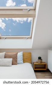Concept of morning light in house. Vertical view of clean skylight in white bedroom interior. Modern apartment with attic window in small room with home decor, green house plants and cushions on bed