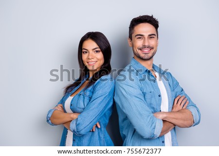 Concept of multiethnic cooperation and friendship. Attractive delightful hispanic woman in denim clothes and handsome causasian smiling man in jeans shirt are standing back to back against  background