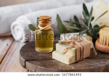 Concept of natural ingredients in cosmetology for gentle skin care. Organic olive oil in glass bottle, handmade soap bars. Atmosphere of serenity and relax. Rustic wooden background, close up.