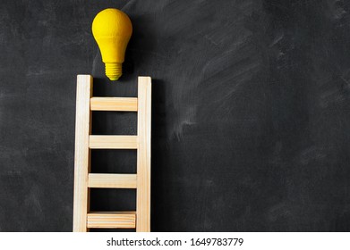 Concept new idea, development, creativity, wooden ladder on black board, yellow light bulb, copy space
