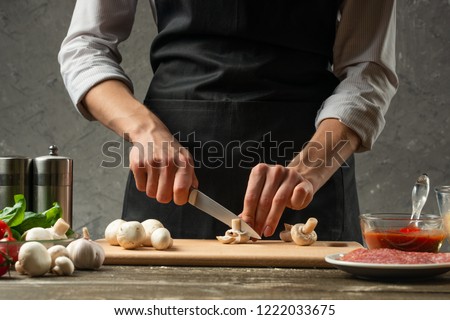 The concept of nutrition. The chef cuts mushrooms on the background of a concrete wall, with ingredients for cooking pizza, pizza sauce, for mushroom soup