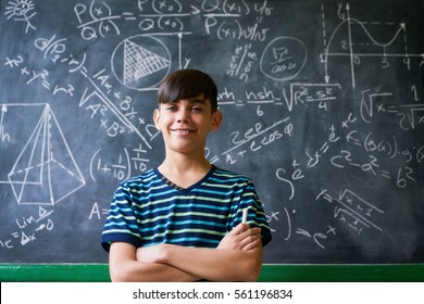 Concept On Blackboard At School. Young People, Student And Pupil In Classroom. Smart Hispanic Boy Writing Math Formula On Board During Lesson. Portrait Of Male Child Smiling, Looking At Camera