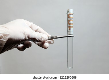 Concept On Corruption And Paid Services In The Field Of Medicine, Science. Left Male Hand Of A Doctor Or Lab Technician In A White Glove Holds Tweezers With A Test Tube With A Hundred Dollars Inside.