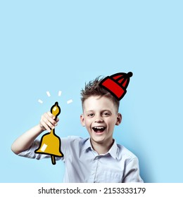 A Concept On The Theme Back To School, A Portrait Of A Laughing Boy In A Light Shirt And Hat Who Rings The School Bell, On A Blue Background.