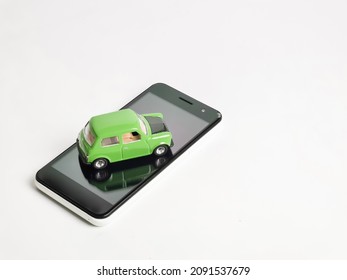 Concept of online application for vehicles. Green toy car on smarphone against white background.