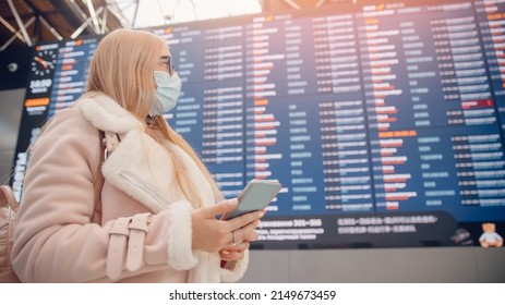 Concept Online Checkin For Plane. Young Woman In Protective Mask With Backpack In Front Of Information Board In Airport Terminal.