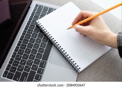 Concept of online learning, language courses, web, education, goals, self-development, recordings for an internet event. Female hand writes with pencil in notebook lying on computer keyboard. 