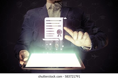 Concept of online learning. Man  touches to certificate icon  (diploma). He  holds tablet pc, that contains a many different online services. - Powered by Shutterstock