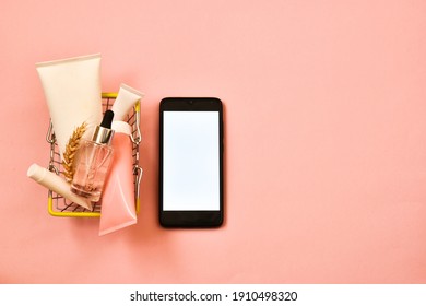 Concept Of Online Shopping Cosmetics. Cosmetics Tubes And Mobile Phone With Shopping Basket From The Supermarket On A Pink Background. Copy Space, Flat Lay.