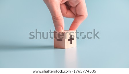 The concept of opposites, hand choose wood blog with plus and minus on blue background, copy space.