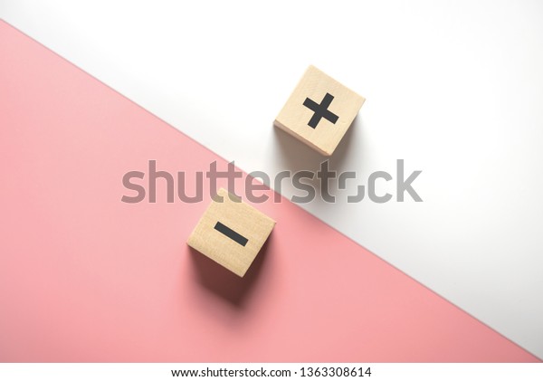 The concept of opposites, wood blog with plus and minus on white and pink background, flat lay, copy space, top view.