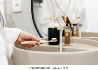 Concept of oral and dental care at home. Cropped shot of woman holding bamboo toothbrush with toothpaste over sink. Female in bathrobe standing in bathroom in morning - Powered by Shutterstock