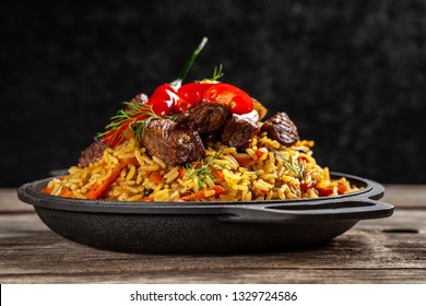 The concept of oriental cuisine. National Uzbek pilaf with meat in a cast-iron skillet, on a wooden table. background image. top view, copy space, flat lay - Powered by Shutterstock