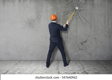 The Concept Of Overcoming Obstacles. Man In Suit And Helmet Hammer Smashes A Barrier. The Notion Of Breaking Down Barriers And Achieve Goals.