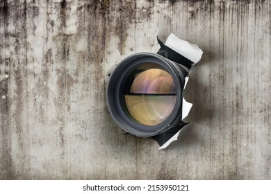 Concept of paparazzi or hidden camera, camera lens looks out through a hole in vintage paper wall
