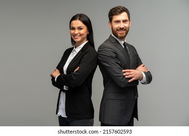 Concept of partnership in business. Young man and woman standing back-to-back with crossed hands against grey background 