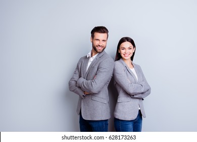 Concept Of Partnership In Business. Young Man And Woman Standing Back-to-back With Crossed Hands Against Gray Background