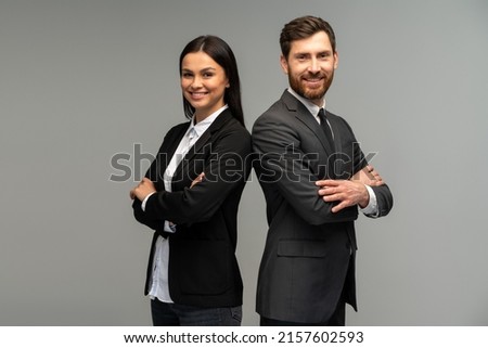 Concept of partnership in business. Young man and woman standing back-to-back with crossed hands against grey background 