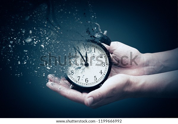 Concept of passing\
away, the clock breaks down into pieces. Hand holding analog clock\
with dispersion effect