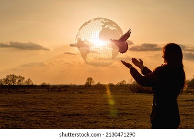 Concept Peaceful Sky On Planet Earth And Hope. A Woman Releases A Dove Against The Background Of A Sunset And A Globe.