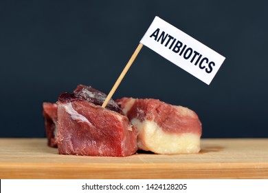 Concept Photo For Antibiotics Residue And Antibiotic Resistance In Meat For Human Consumption, Showing Chunk Of Red Meat With Flag On Wooden Board