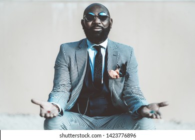 A concept photo with an elegant bald bearded black man in a suit with tie and round sunglasses from the matrix offering to make a choice with red and blue pills in his hands - Powered by Shutterstock