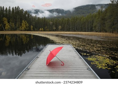 A concept photo of a red umbrella resting on a small dock at Sinclair Lake in the far north part of Idaho during autumn.