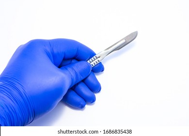 Concept photo surgery and surgical treatment, operations, procedures. Doctor holds in his hand, dressed in blue medical glove, metal scalpel with removable blade on white homogeneous background