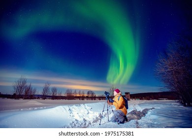 Concept photo tour to arctic travel, photographer man with camera and tripod photographs aurora borealis, northern lights green.