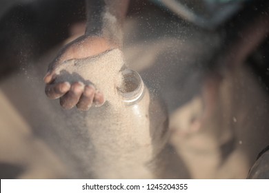 Concept Photography, Eco Building: Aerial Close Up  African Man Hand Filling Up With Sand A Plastic Water Bottle, Making Ecobrick, Outdoors On A Sunny Summer Day, In Gambia, Africa On Atlantic Beach