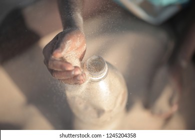 Concept Photography, Eco Building: Aerial Close Up  African Man Hand Filling Up With Sand A Plastic Water Bottle, Making Ecobrick, Outdoors On A Sunny Summer Day, In Gambia, Africa On Atlantic Beach