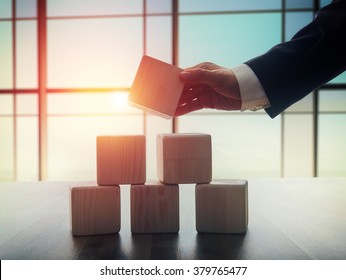 The concept of planning in business. Wooden cubes on a desk in the office. The concept of leadership. Hand men in business suit holding the cubes.
