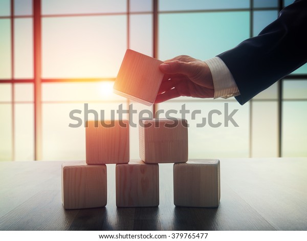 The concept of planning in business.\
Wooden cubes on a desk in the office. The concept of leadership.\
Hand men in business suit holding the\
cubes.