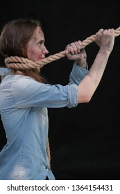 Concept Portrait Of Offended, Displeased, Dirty, Sharpened In Captivity Brunette Girl On A Black Background, Bound By A Rope. Violence Against Women. You Have No Chance To Help Her, Let Her Go.