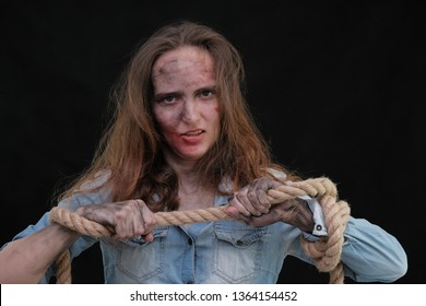 Concept Portrait Of Offended, Displeased, Dirty, Sharpened In Captivity Brunette Girl On A Black Background, Bound By A Rope. Violence Against Women. You Have No Chance To Help Her, Let Her Go.