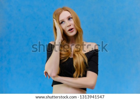 Concept portrait of a pretty beautiful red-haired girl talking on a blue background in the studio standing in front of the camera. It shows different emotions in different poses.