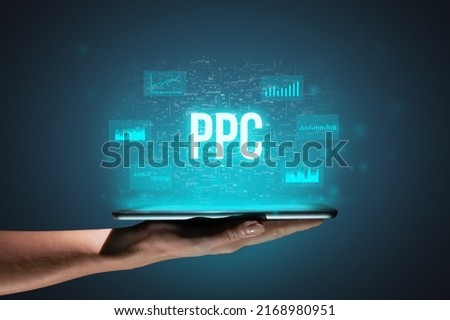 Concept PPC or Pay per click. Business acronym. Holographic icons and text over tablet in hands.