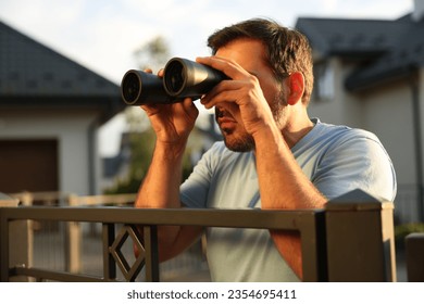 Concept of private life. Curious man with binoculars spying on neighbours over fence outdoors - Powered by Shutterstock