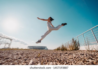 Concept of promoting a healthy lifestyle and good mood. Fitness or gymnast or dancer doing exercises near the city stadium. performs dance jumps from bottom