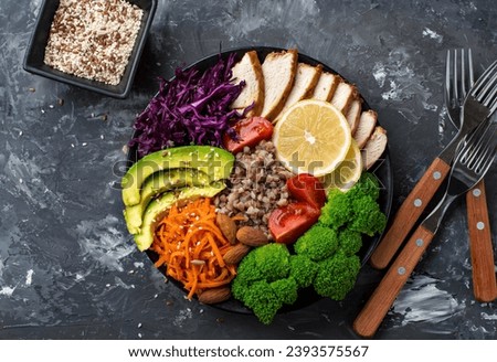 The concept of proper, nutritious nutrition, a bowl with chicken breast, buckwheat, vegetables, cabbage, broccoli, carrots, nuts, avacado and cherry tomatoes on a dark background.