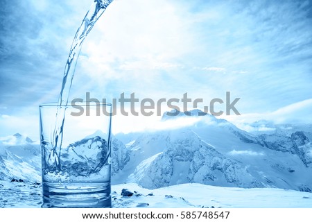 concept purity of blue water in transparent glass over winter landscape of mountains higher than clouds, close up
