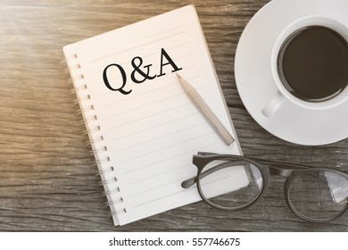 Concept Q&A message on notebook with glasses, pencil and coffee cup on wooden table.