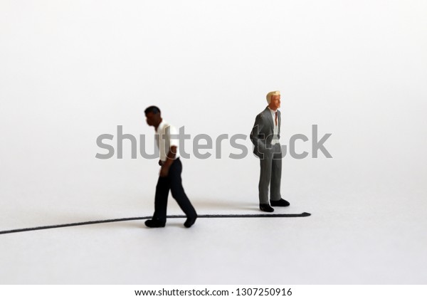The concept of racial conflict. A miniature black\
man and a miniature white man standing back from each other with\
boundaries between them.