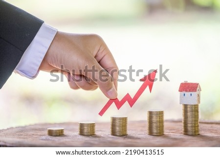 Concept of real estate investment.Business growth.House on a pile of coins.Stack of coins arranged in ascending order.The investor's hand catches the red arrow.Business investment ideas.