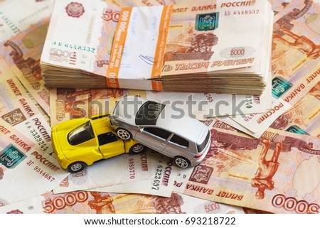 The concept of receipt of insurance premium after car accident: two toy cars and a stack of Russian rubles in the banking package lying on the background of scattered banknotes