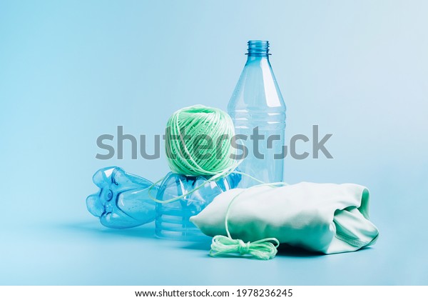 The\
concept recycling plastic. Empty plastic bottle and recycled\
polyester fiber, synthetic fabric blue\
background