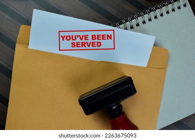 Concept of Red Handle Rubber Stamper and You've been Served text above from brown envelope isolated on on Wooden Table.