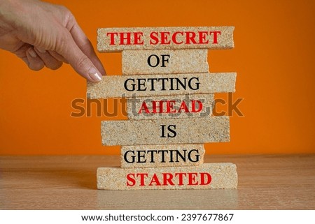 Concept red words The Secret Of Getting Ahead Is Getting Started on brick blocks. Beautiful wooden table, orange background. Businessman hand. Concept inspirational quote of the day. Copy space.