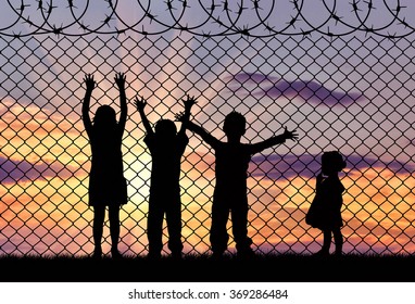 Concept Of Refugee. Silhouette Of The Hungry Children Of Refugees Near The Border Fence In The Sunset