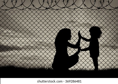 Concept Of Refugee. Silhouette Of Mother And Child Refugees At The Border Fence At Sunset